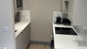 Uma cozinha compacta com armários brancos, micro-ondas, máquina de café e forno embutido.
