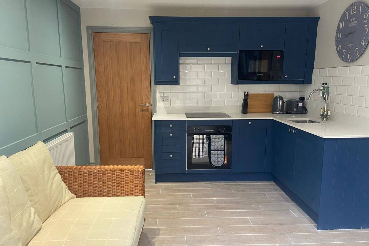 A compact kitchen with blue cabinets, a microwave, and a built-in oven.