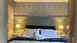 A hotel room with a bed, two bedside lamps, a ceiling fan, and patterned wallpaper. - Durham City Cottages (Durham)