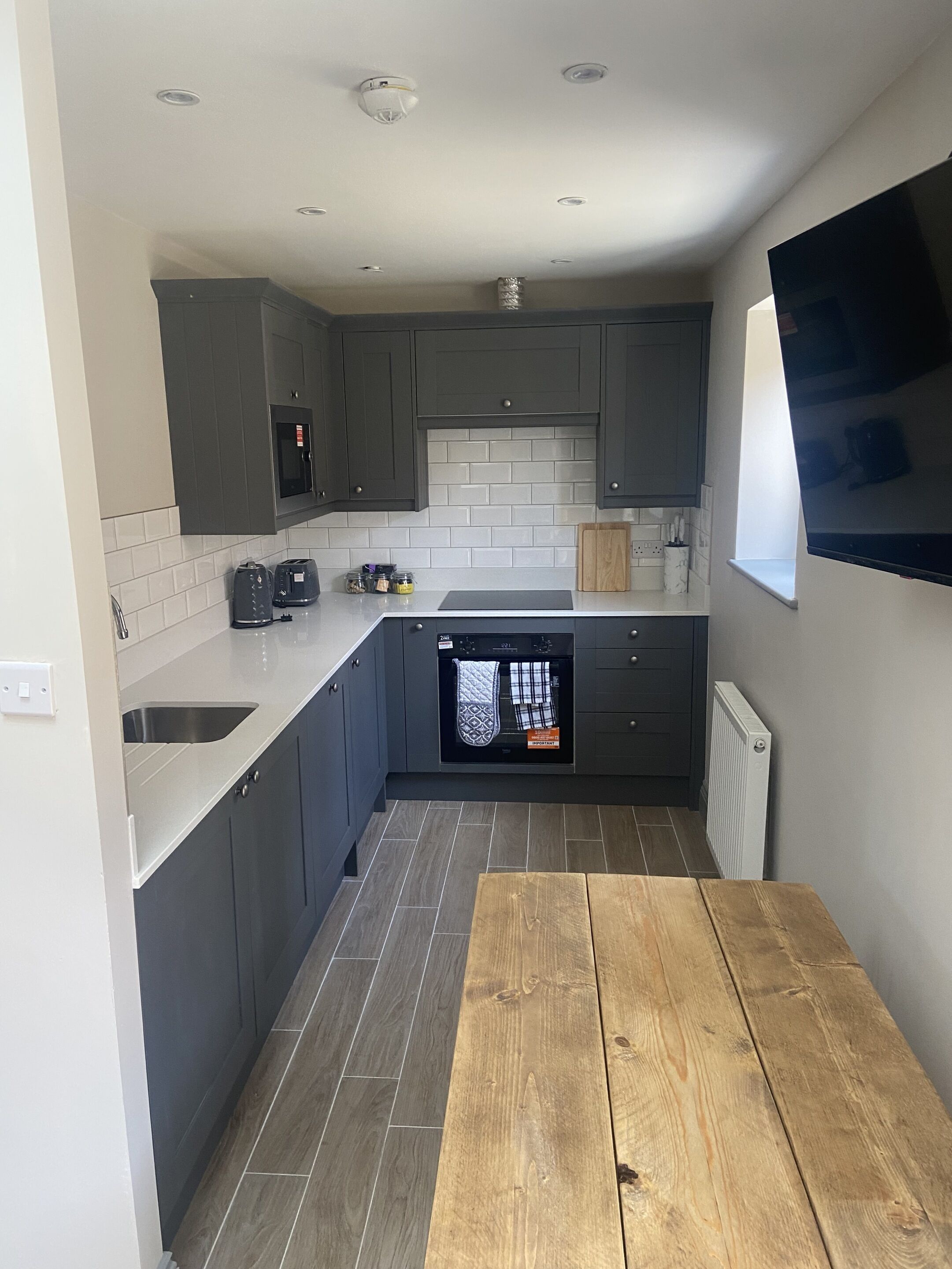 A compact kitchen with grey cabinets, a built-in oven, and a wooden table.