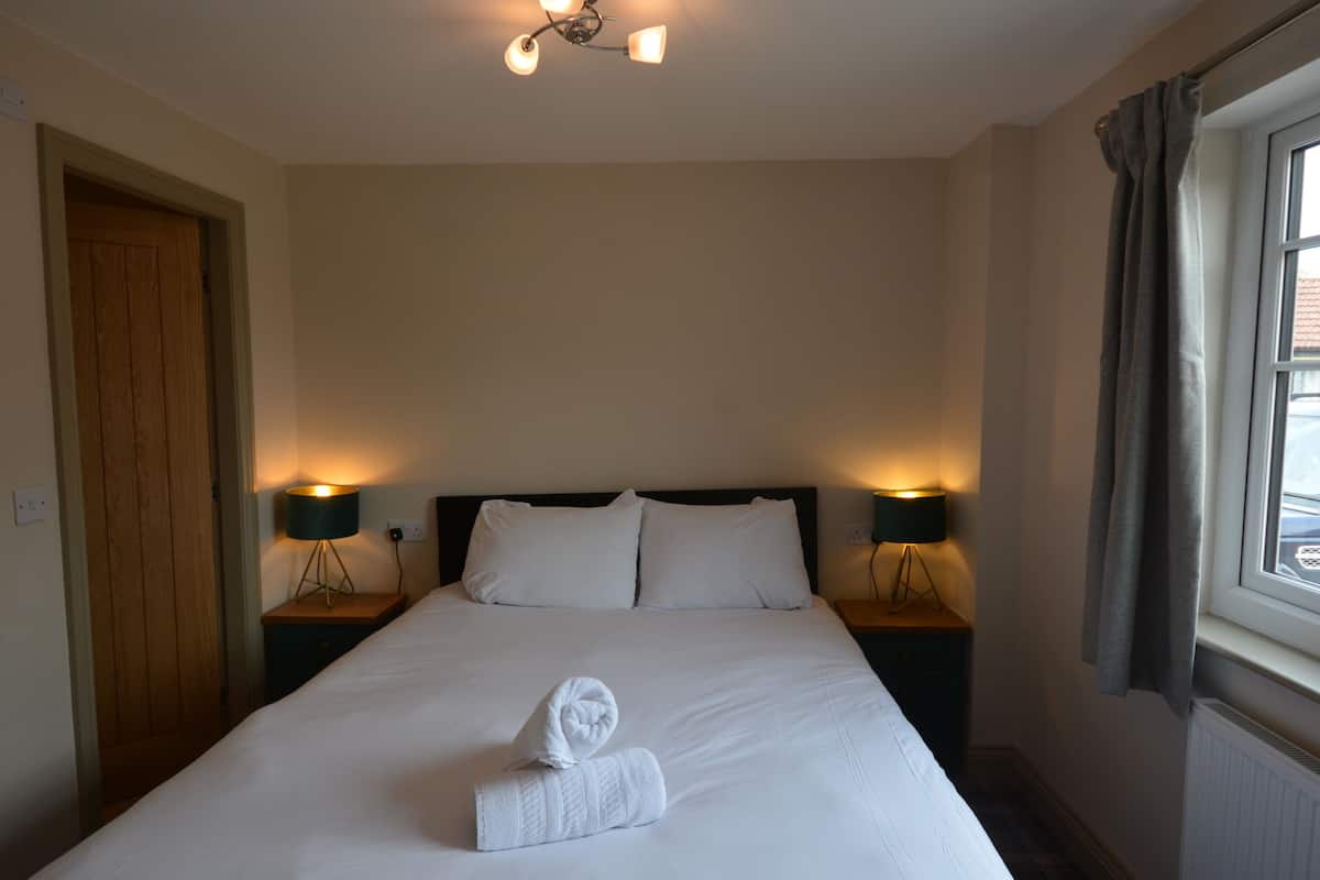 A hotel room with a large bed, two bedside lamps, a wooden door, and a window with curtains.