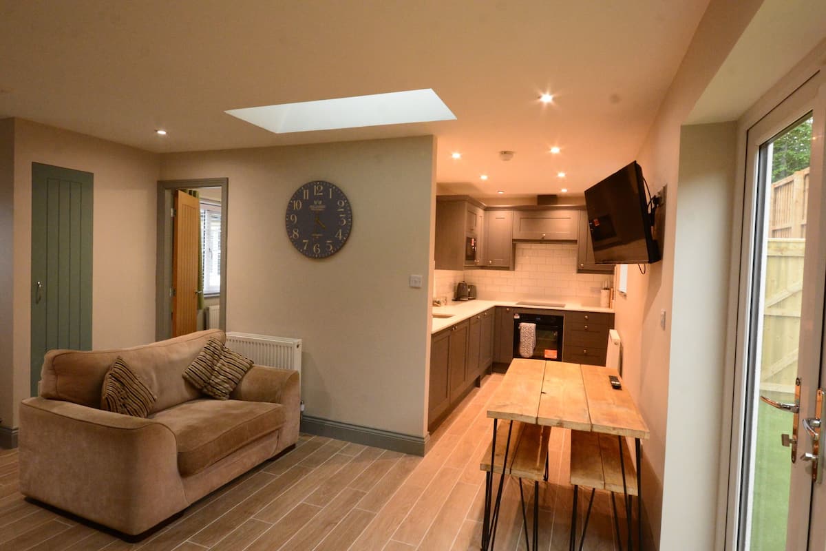 A compact living space with a sofa, a dining table, a kitchen area, and a flat-screen TV mounted on the wall.
