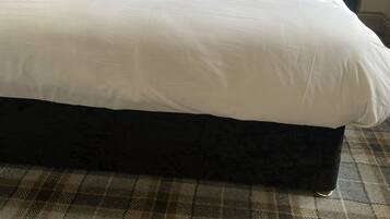 Una cama bien hecha con sábanas blancas y una toalla enrollada, flanqueada por dos lámparas verdes sobre mesitas de noche.