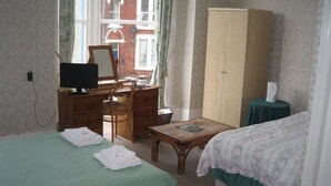 Une chambre avec deux lits, un bureau avec un ordinateur, une armoire et une fenêtre avec des rideaux.