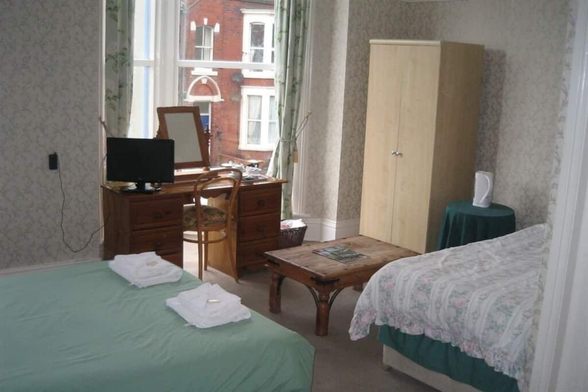 A room with two beds, a desk with a computer, a wardrobe, and a window with curtains.
