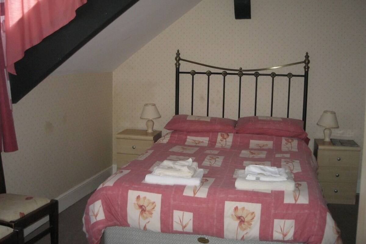 A bedroom with a metal bed frame, a pink floral bedspread, two bedside tables with lamps, and a chair.