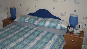 Une chambre à coucher avec un lit, deux oreillers, une table de chevet avec une lampe, une machine à café et une petite table avec des articles de toilette.