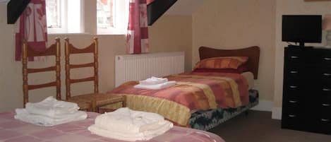 A bedroom with two beds, a wooden chair, a radiator, a black dresser, and a window with curtains.