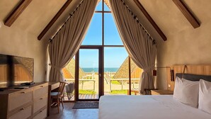 A bedroom with a large window, wooden ceiling beams, a bed, a desk, and a chair.