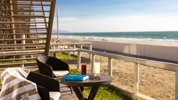 Un espacio de descanso frente al mar, con vistas al océano, una mesa con una bebida y un libro, y una silla de mimbre con una toalla a rayas.