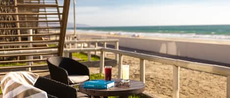 Un espacio de descanso frente al mar, con vistas al océano, una mesa con una bebida y un libro, y una silla de mimbre con una toalla a rayas.