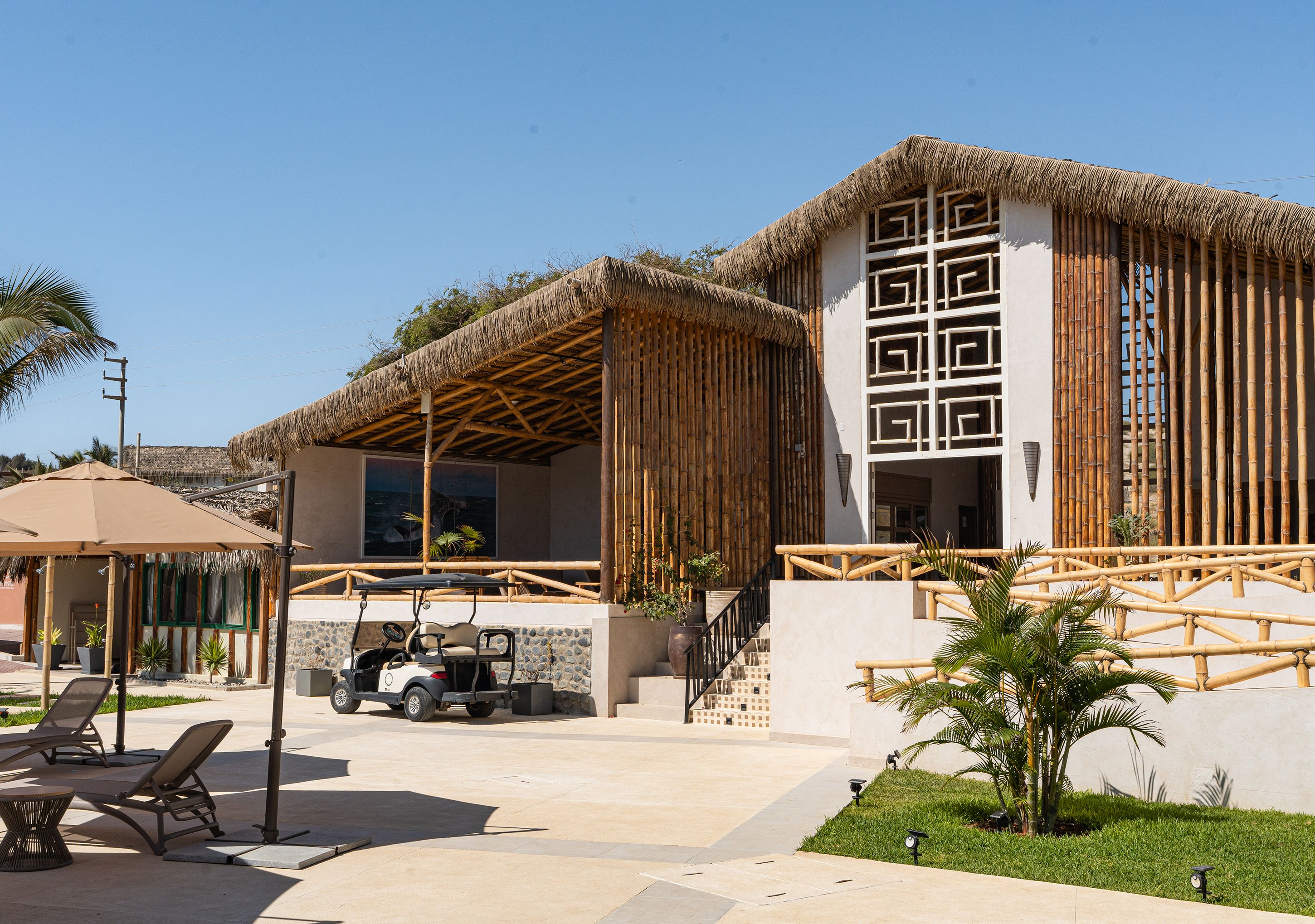 A resort with a thatched-roof building, outdoor seating, and a golf cart.
