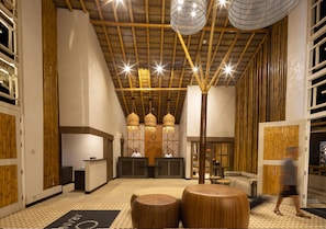 Un área de recepción con techo de bambú, mostrador de recepción y zona de estar con taburetes de madera redondos.