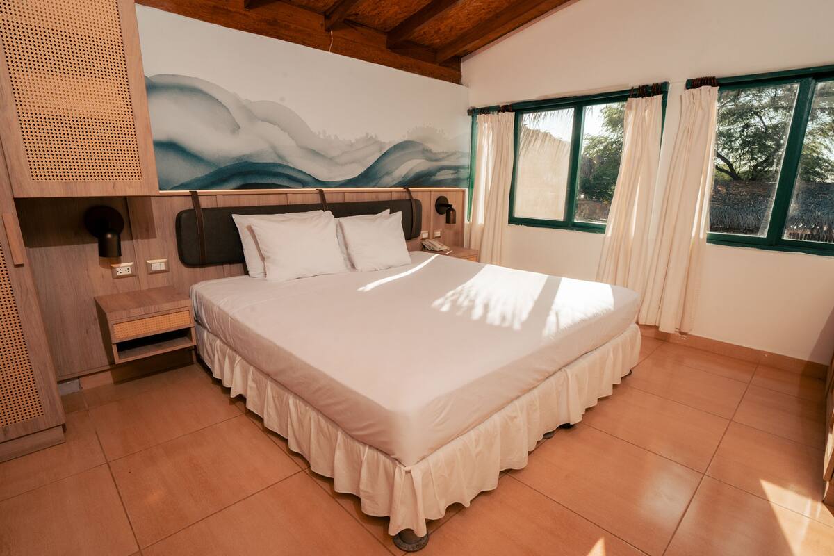 Un dormitorio con una cama grande, cabecera de madera, teléfono en la pared y una ventana con cortinas.