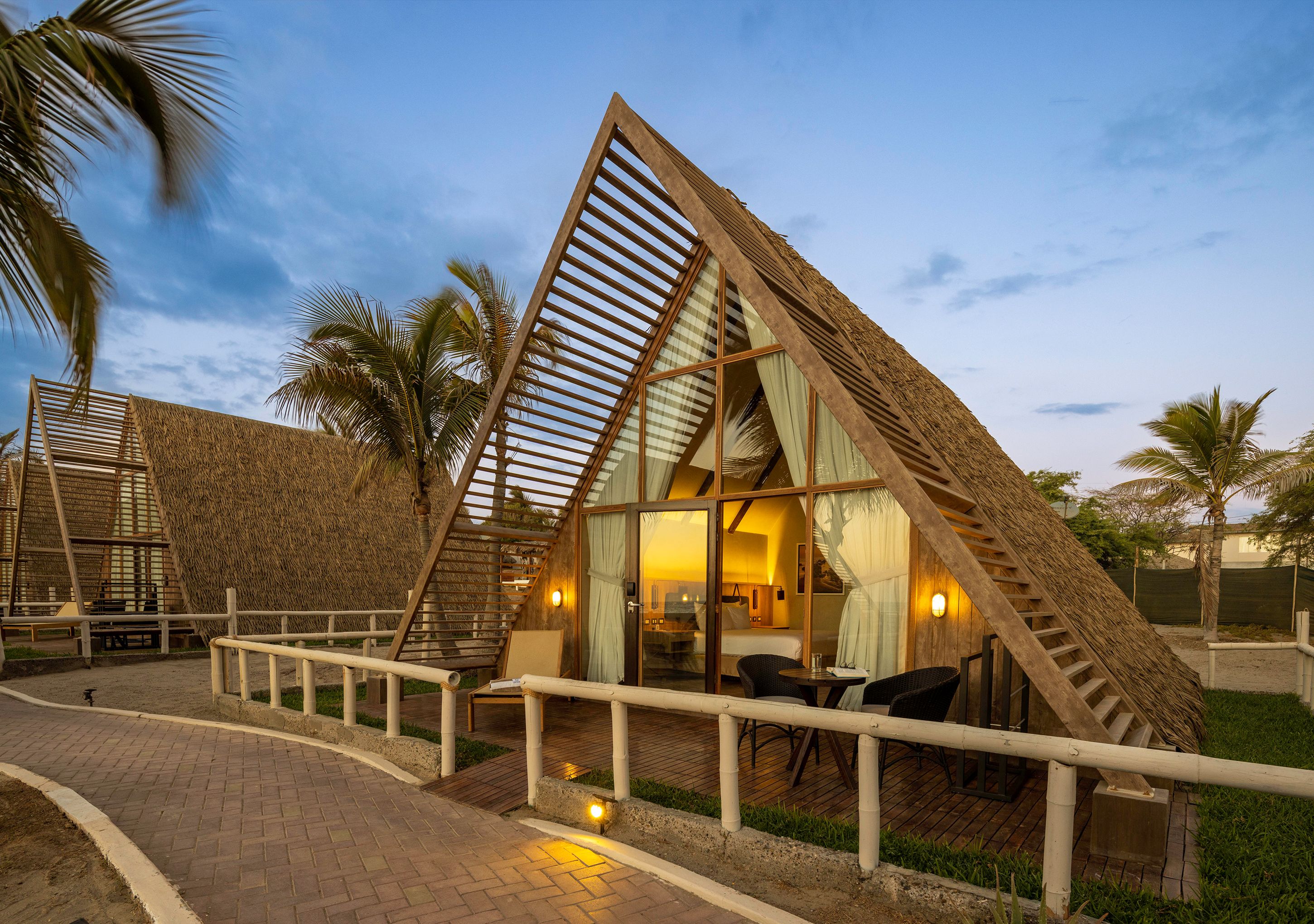 A triangular-shaped building with a thatched roof, large windows, and a balcony with seating.