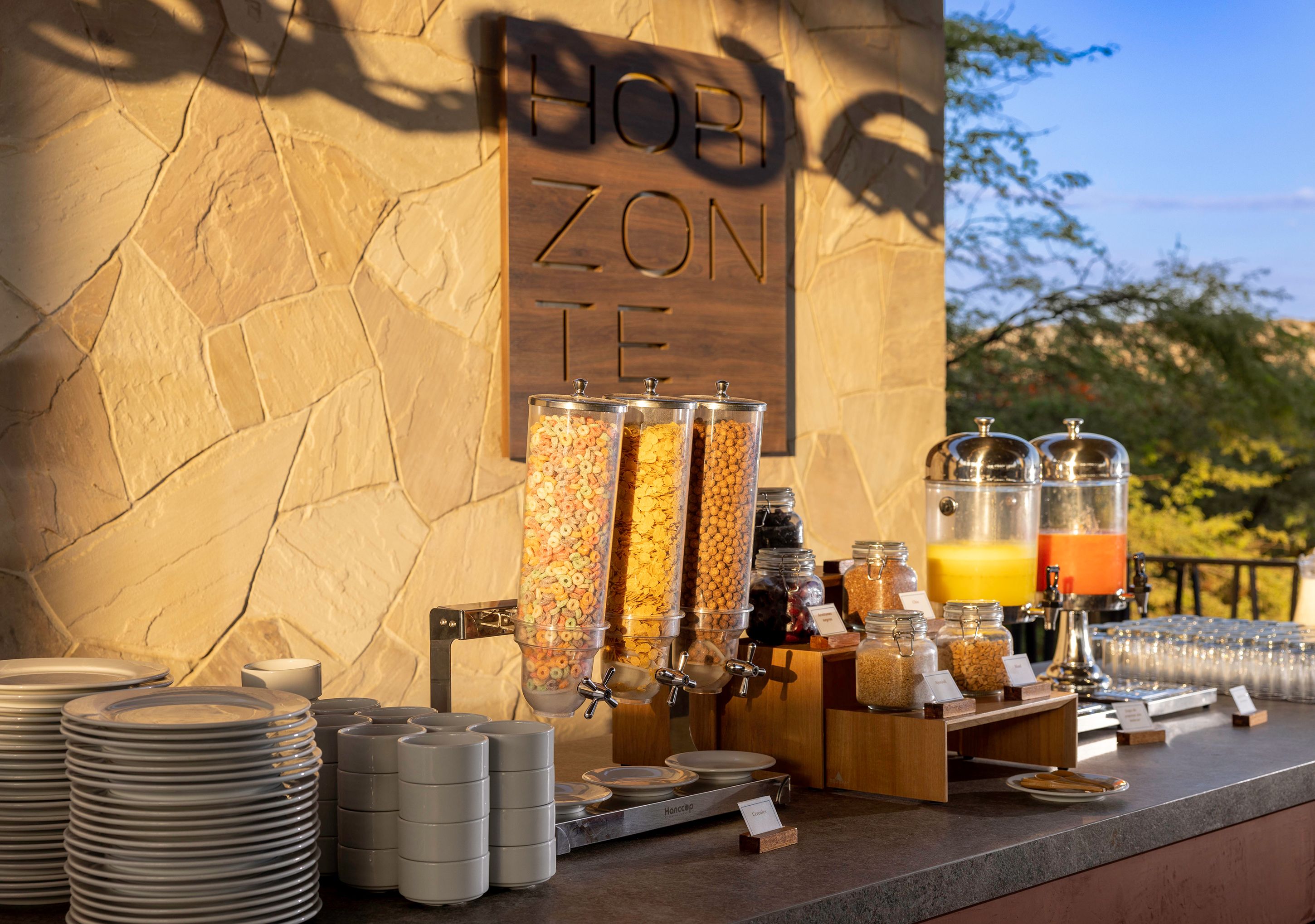 Un bufé de desayuno con dispensadores de cereales y zumos, y un letrero que dice 'HOBBY ZONE'.
