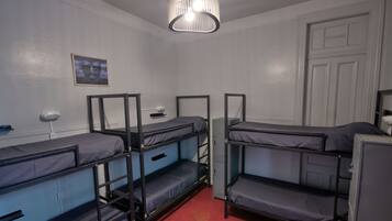 Una habitación tipo dormitorio con literas, un escritorio pequeño, una silla, un calentador y una puerta.