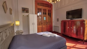 A hotel room with a bed, a television, a wardrobe, a desk, and a chandelier. - Play Hostel Arcos (Buenos Aires)