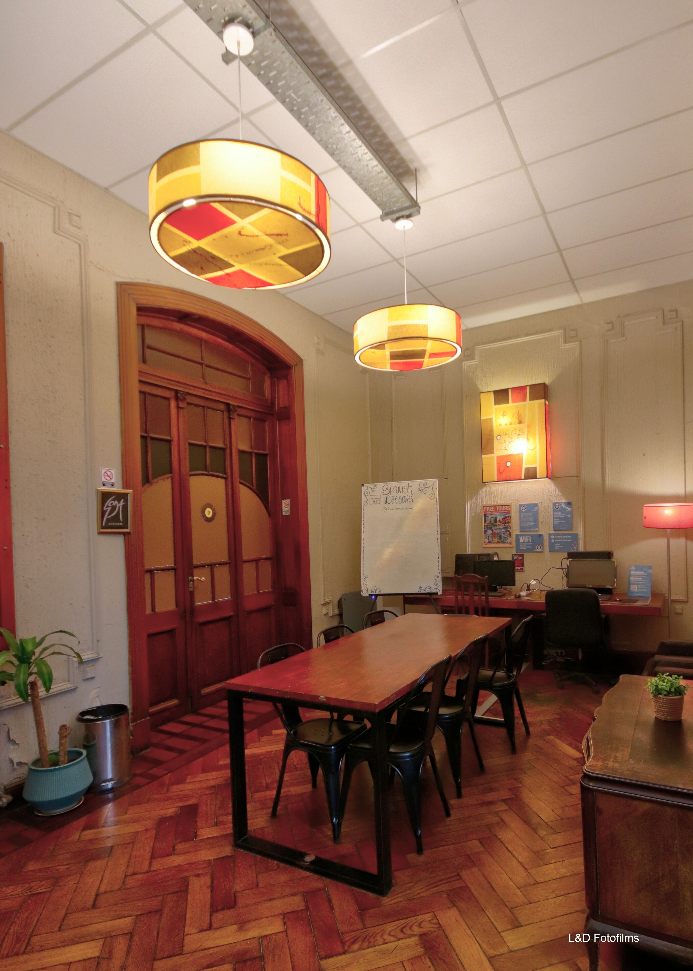 A conference room with a long wooden table, black chairs, a whiteboard, and a red door.