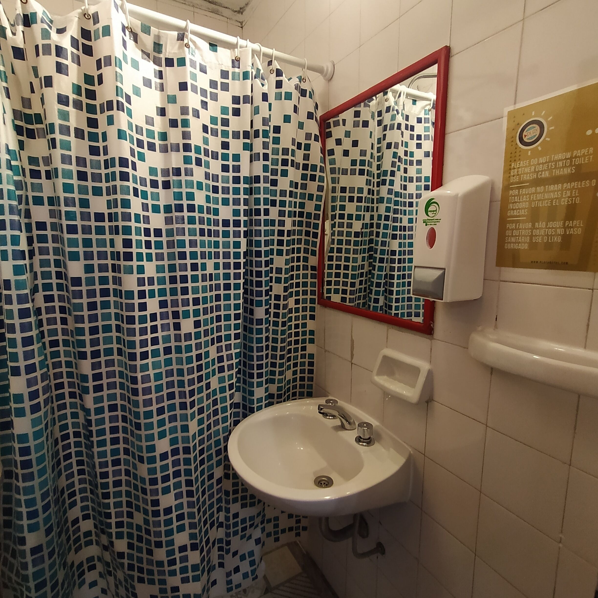 Un baño con cortina de ducha con diseño de mosaico, un lavamanos blanco con un espejo encima y un dispensador de jabón en la pared.