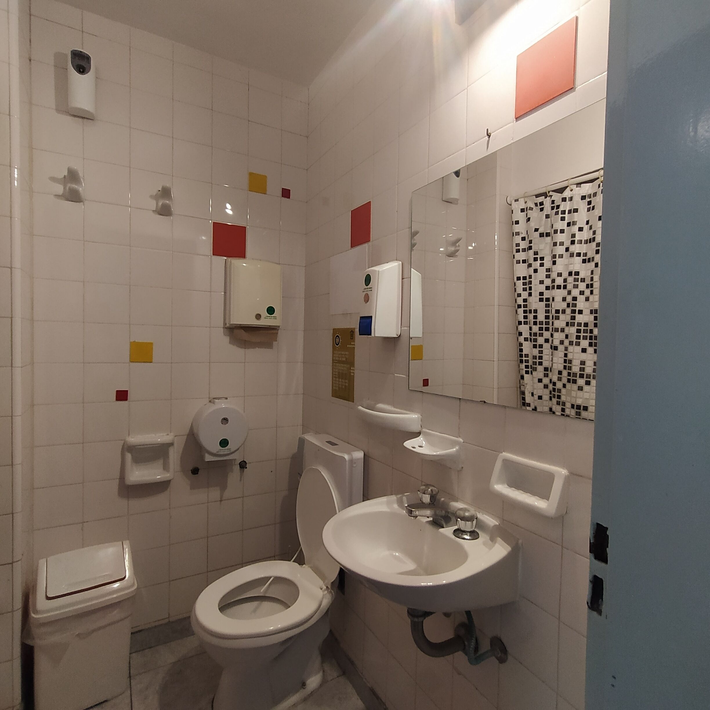 Ein Badezimmer mit Toilette, Waschbecken und Spiegel. An der Wand befinden sich Seifenspender und ein Papiertuchspender.