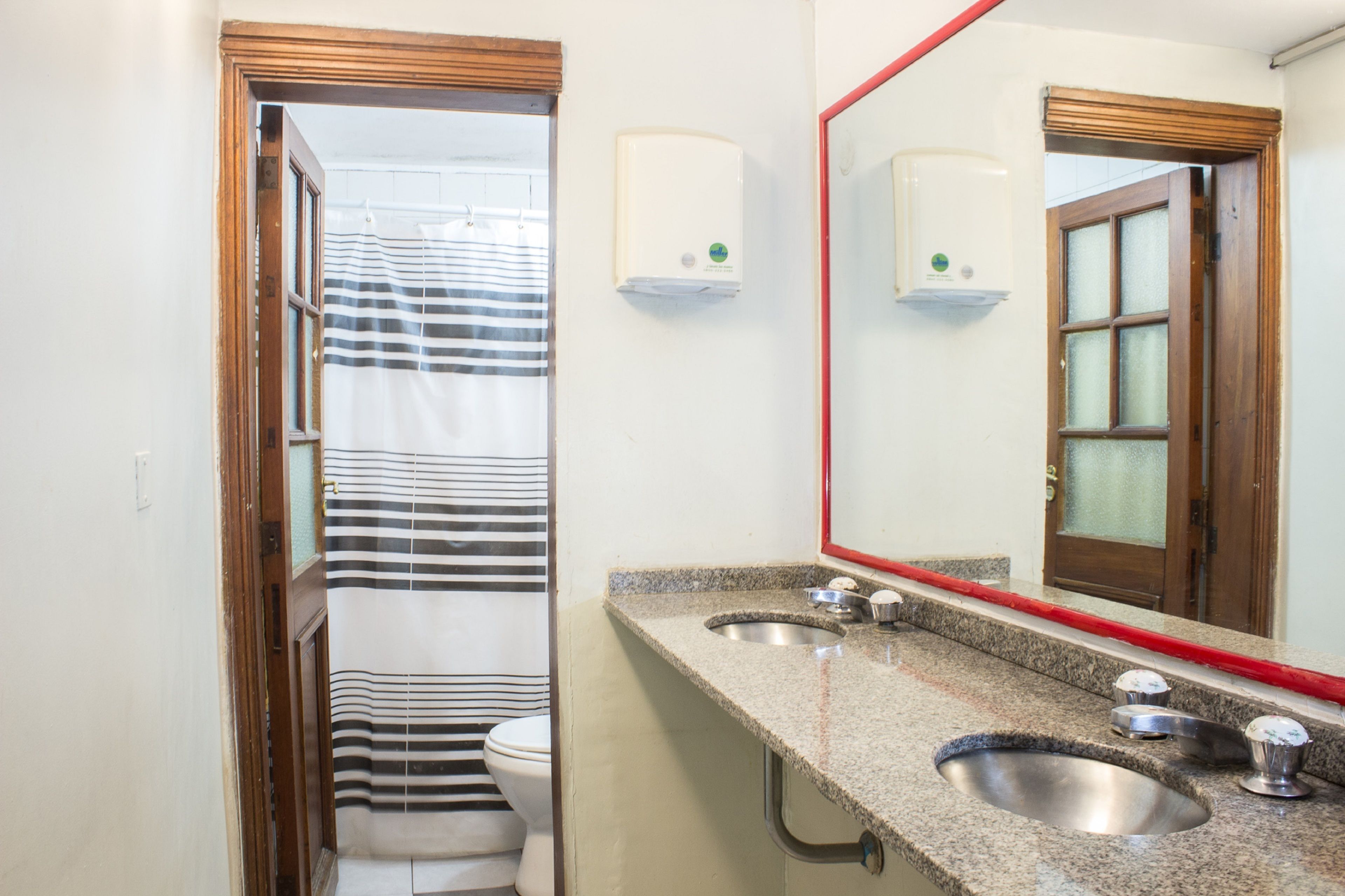 Un baño con dos lavamanos, una cortina de ducha a rayas y un espejo con marco rojo.