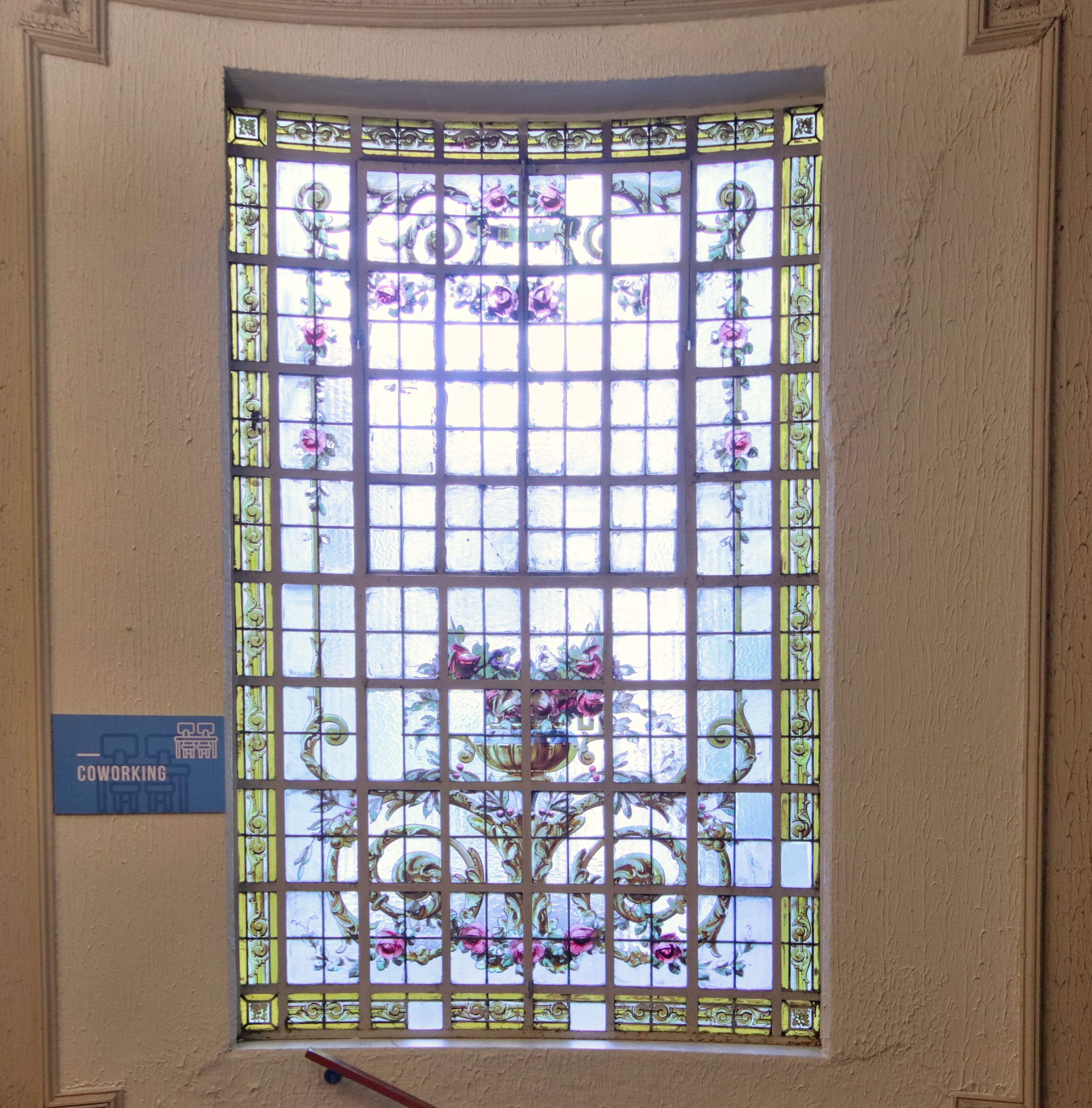 A stained glass window with floral patterns and a sign indicating a coworking space.