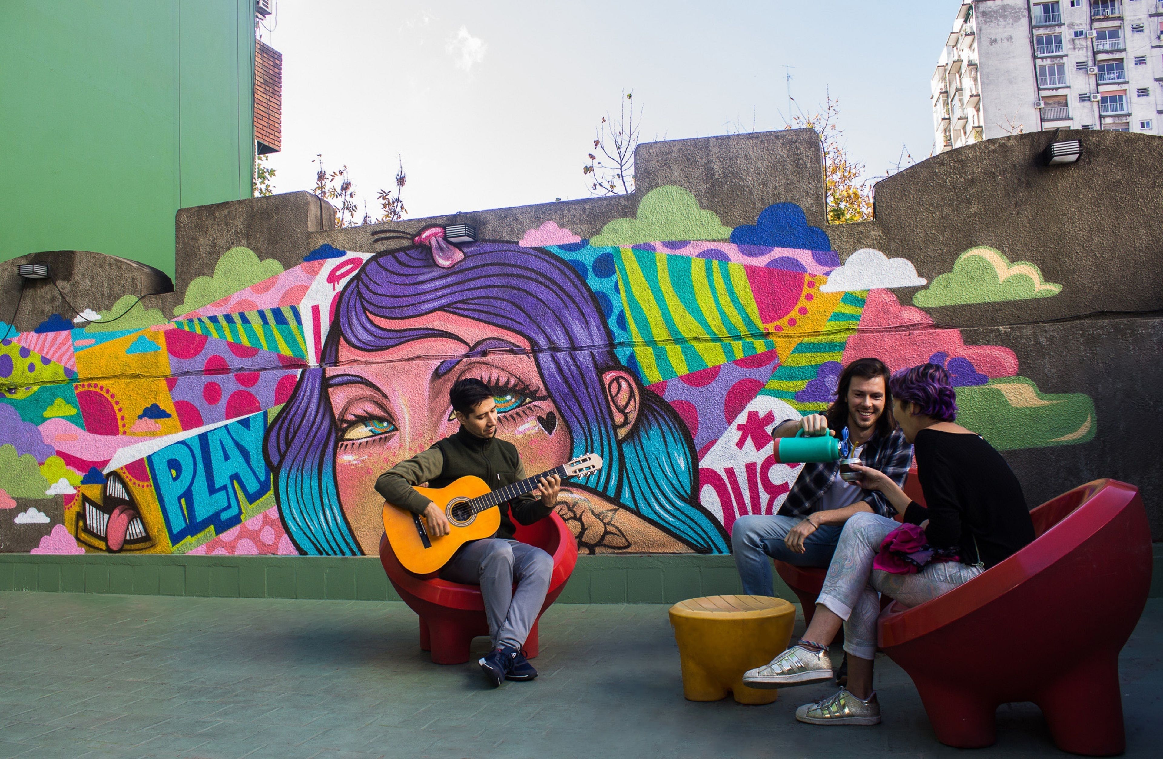 A mural with a guitar player and two seated individuals in an urban outdoor setting.