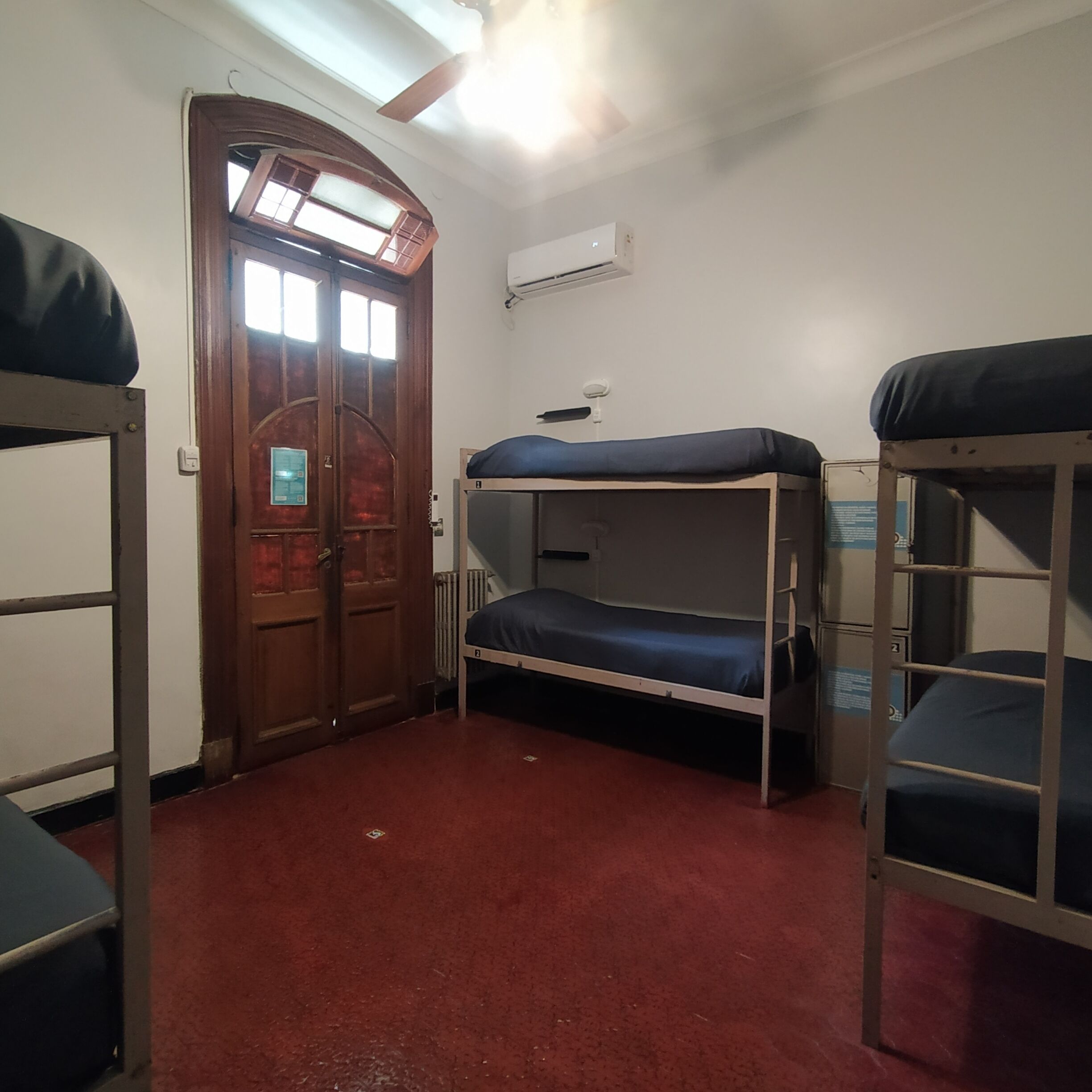 A dormitory room with bunk beds, a wooden door, and a ceiling fan.