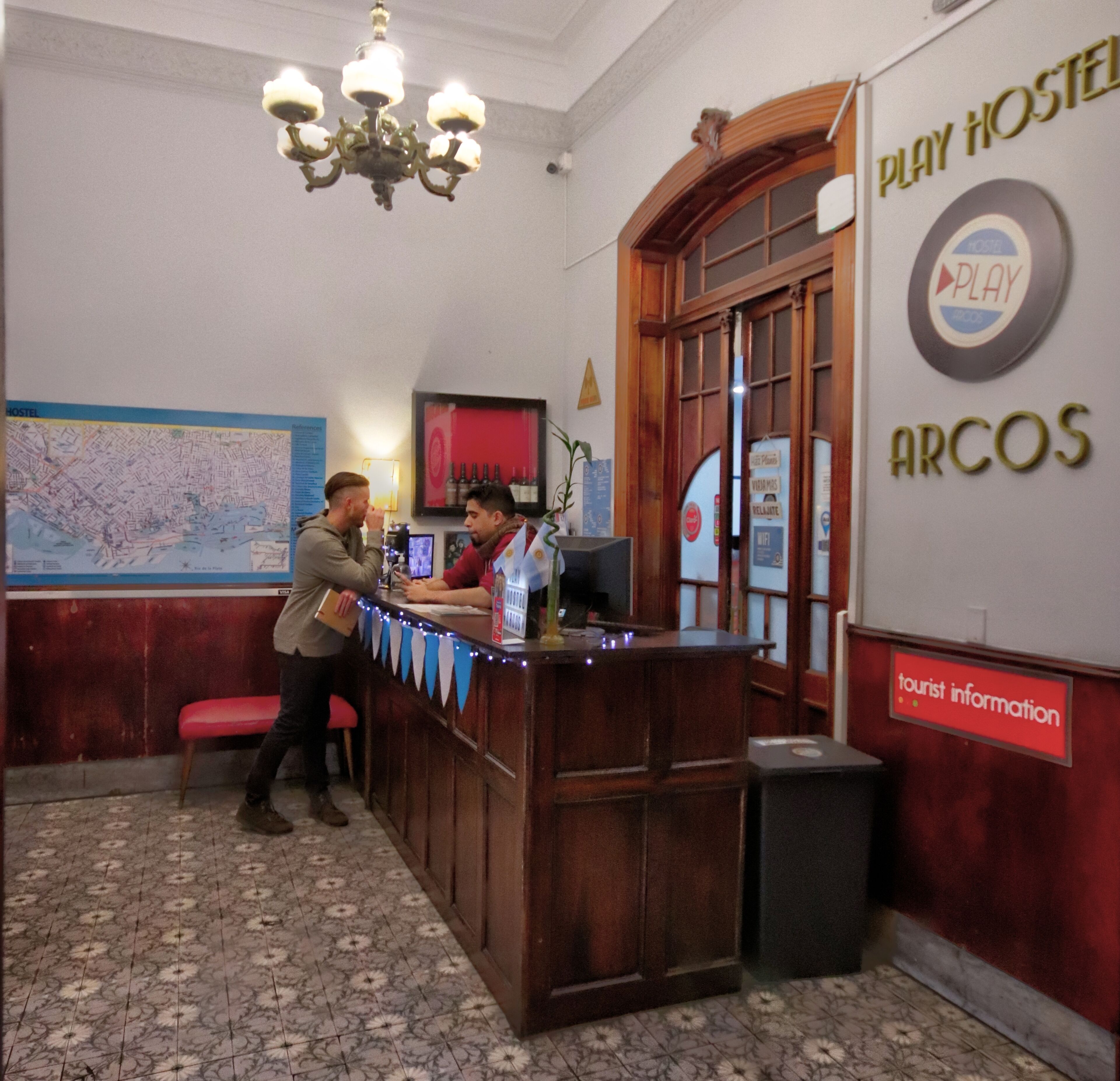 Ein Empfangsschalter mit einer Karte an der Wand, einer Kristallleuchter und Schildern für Play Hostel und touristische Informationen.