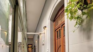 A corridor with a wooden door, a hanging plant, and a tiled floor. - Play Hostel Arcos (Buenos Aires)