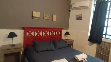 Una habitación de hotel con cama, dos mesitas de noche, cabecera roja y ventana con cortinas.