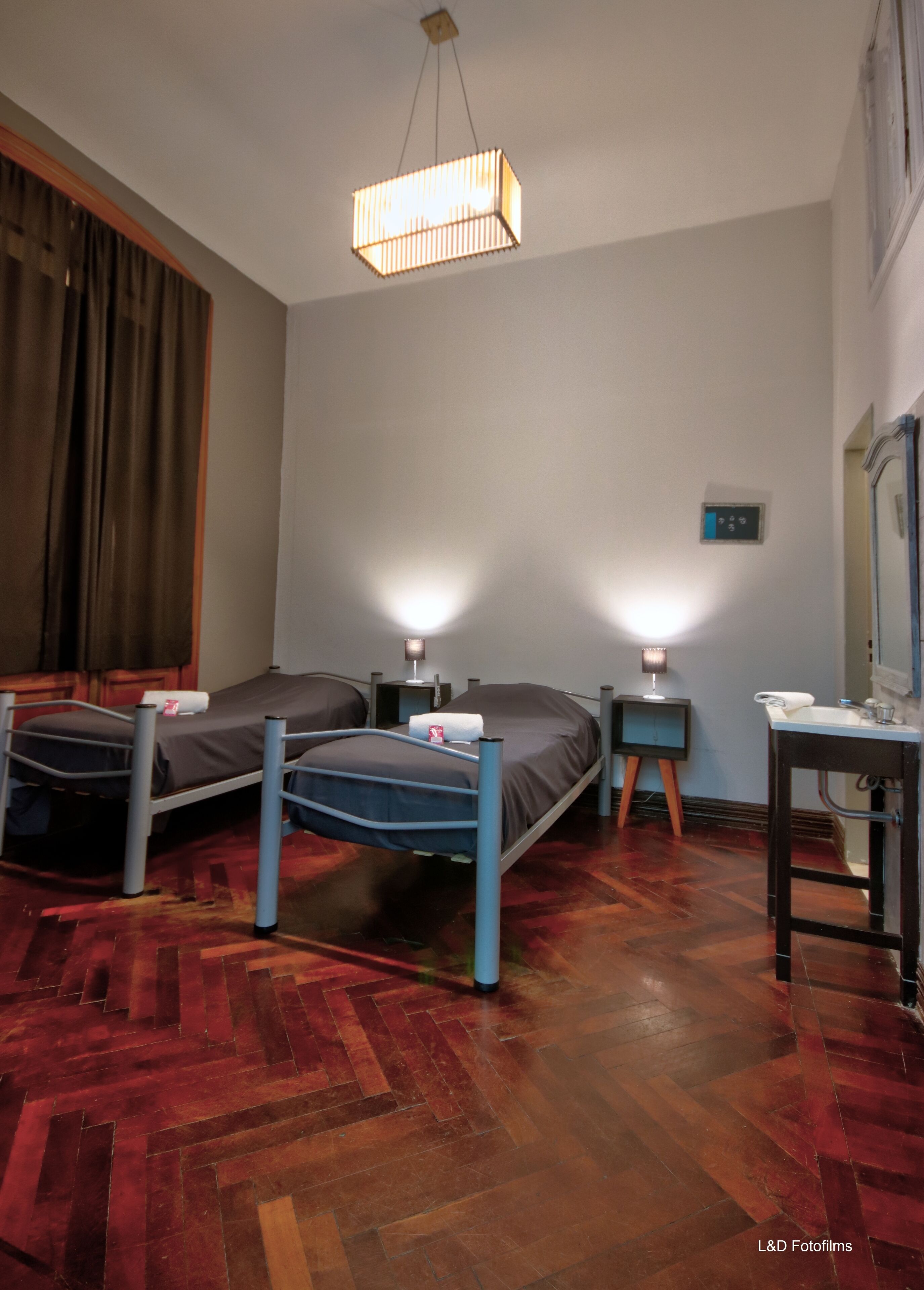 Habitación de hotel con dos camas, un escritorio, una silla, un espejo, una mesita de noche, una lámpara y una lámpara de techo.