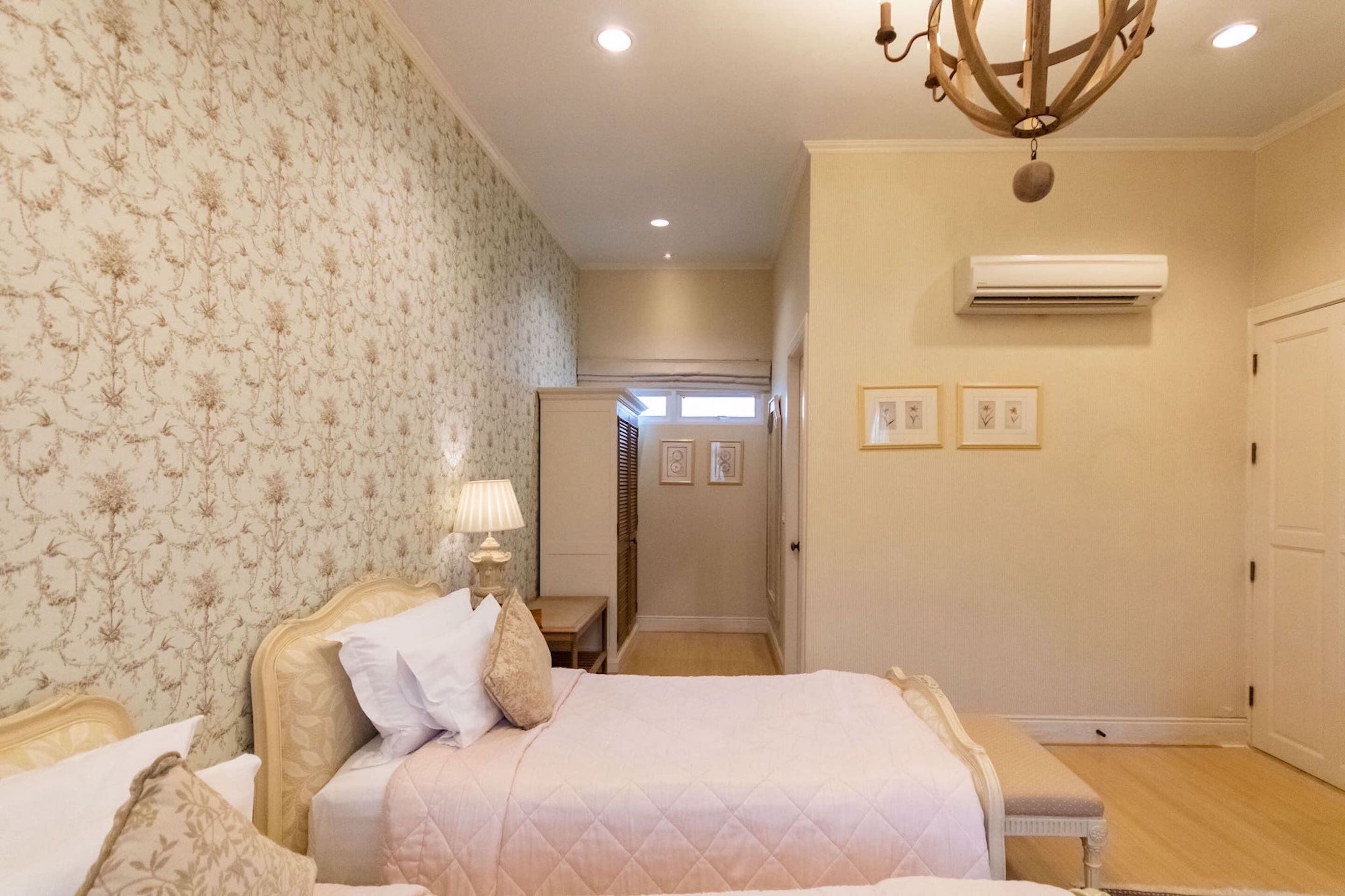 A bedroom with a bed, bedside table, lamp, and an air conditioning unit.