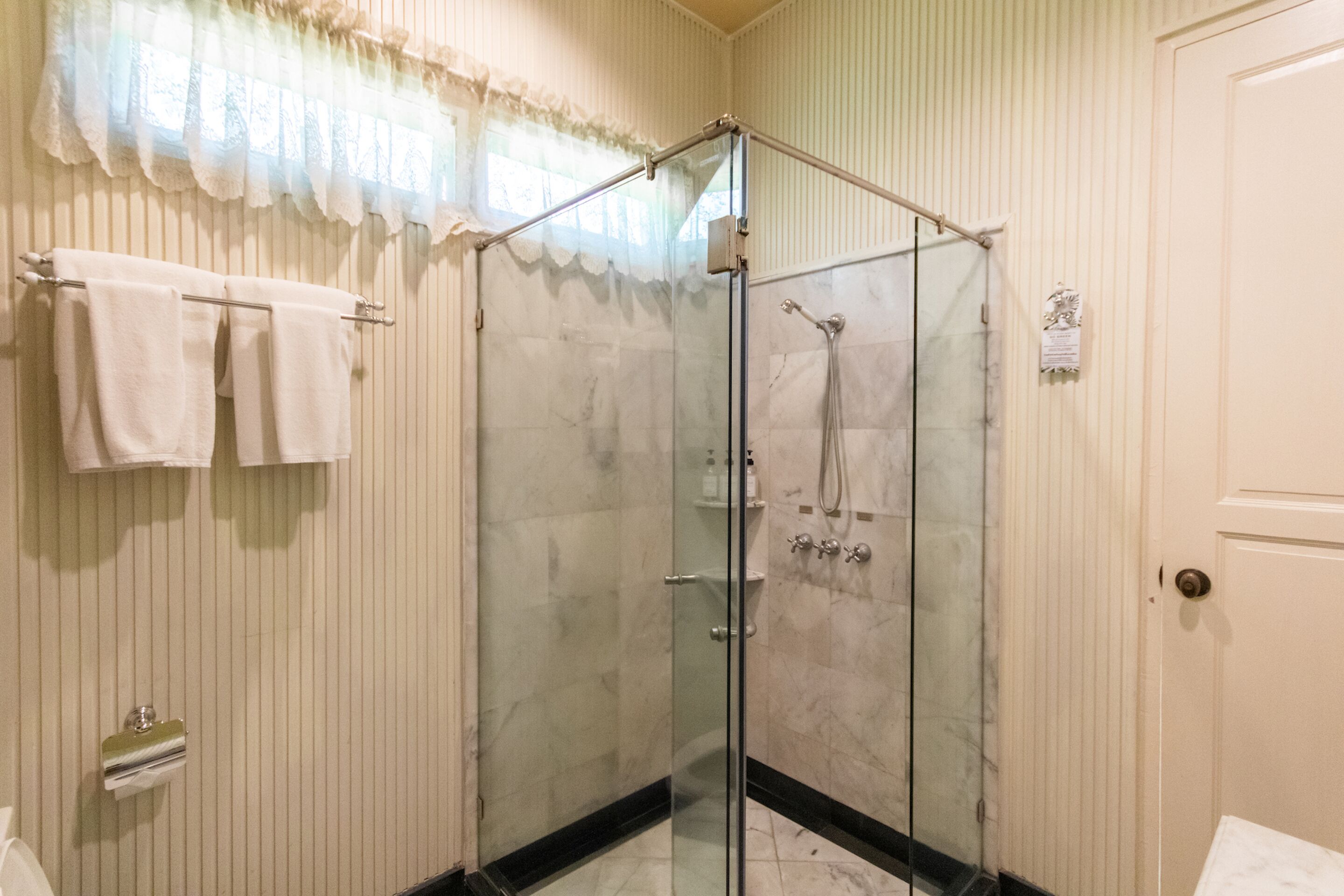 A glass-enclosed shower with a handheld showerhead, a towel rack with towels, and a door with a handle.