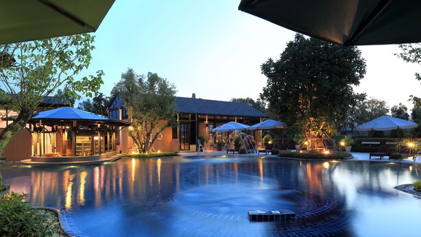 A serene pool area with a circular design, surrounded by lounge chairs and umbrellas, and a building with a modern architectural style. - Rancho Charnvee Khaoyai (Pak Chong)