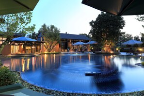 A serene pool area with a circular design, surrounded by lounge chairs and umbrellas, and a building with a modern architectural style. - Rancho Charnvee Khaoyai (Pak Chong)