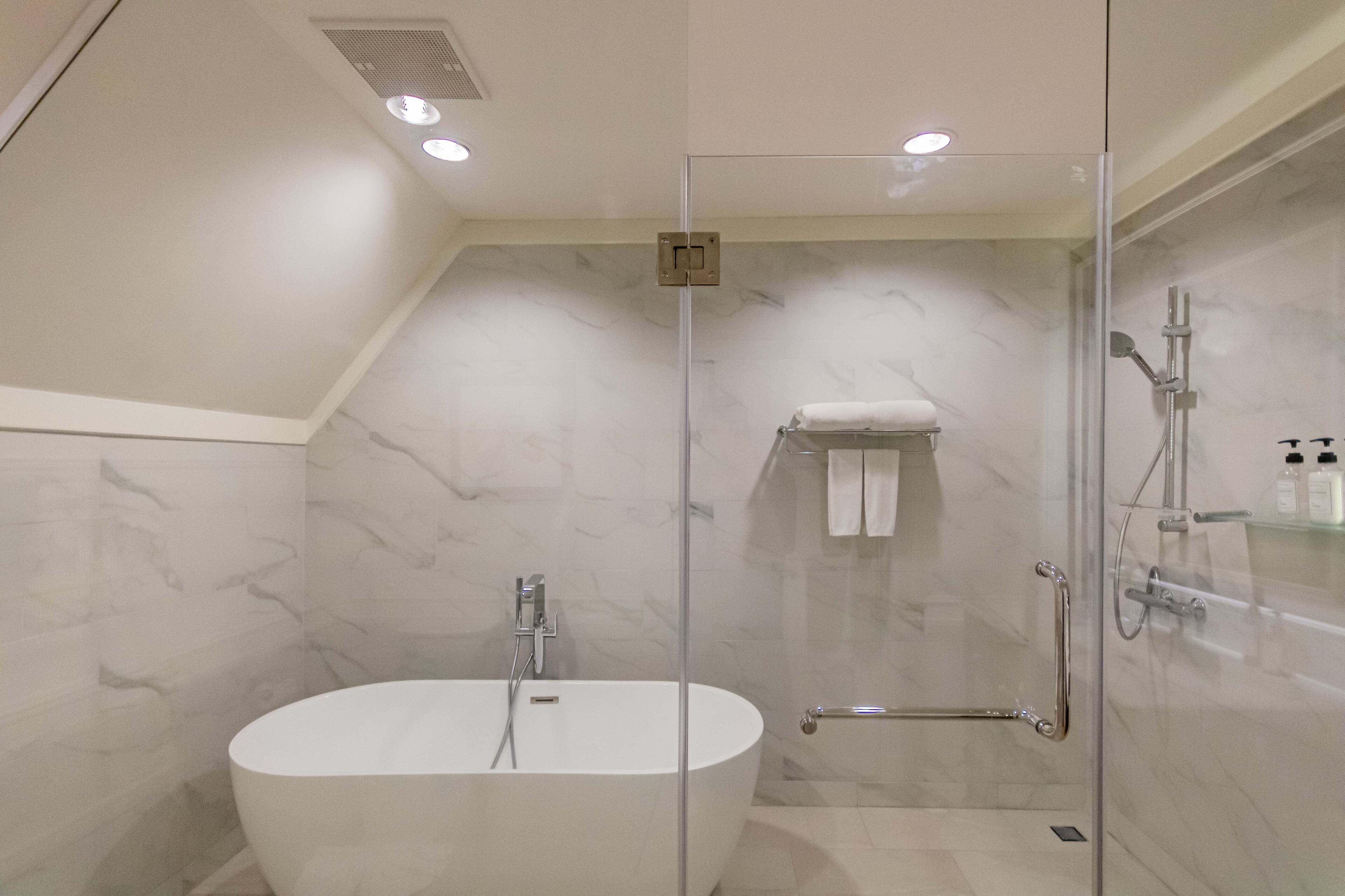 A modern bathroom with a freestanding bathtub, a glass-enclosed shower, and a marble-tiled wall.
