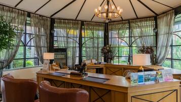 A reception desk with a chandelier, leather chairs, and a view of greenery through large windows.