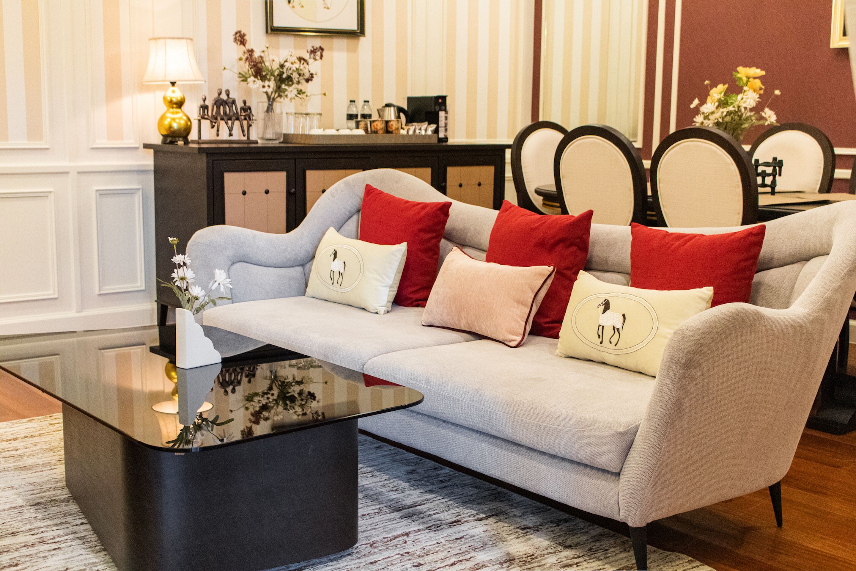 A modern living room with a grey sofa, red and white cushions, a black coffee table, and a floral vase.