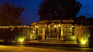 A reception area with a glass facade, steps leading up to it, and a large tree in the background. - Rancho Charnvee Khaoyai (Pak Chong)