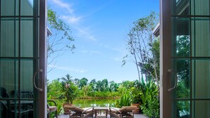 An open deck with outdoor furniture and a view of a pond surrounded by lush greenery. - Rancho Charnvee Khaoyai (Pak Chong)