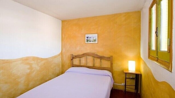 A single bed with a wooden headboard in a room with yellow walls and a small bedside table with a lamp. - Casa Pueblo Hostel (Mendoza)