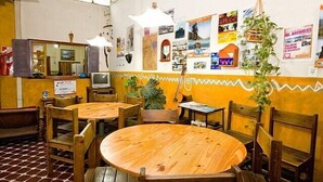 A restaurant with wooden tables and chairs, a tiled floor, and a wall decorated with various pictures and posters. - Casa Pueblo Hostel (Mendoza)