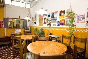 Um restaurante com mesas e cadeiras de madeira, chão de azulejos e parede decorada com diversas fotos e cartazes.