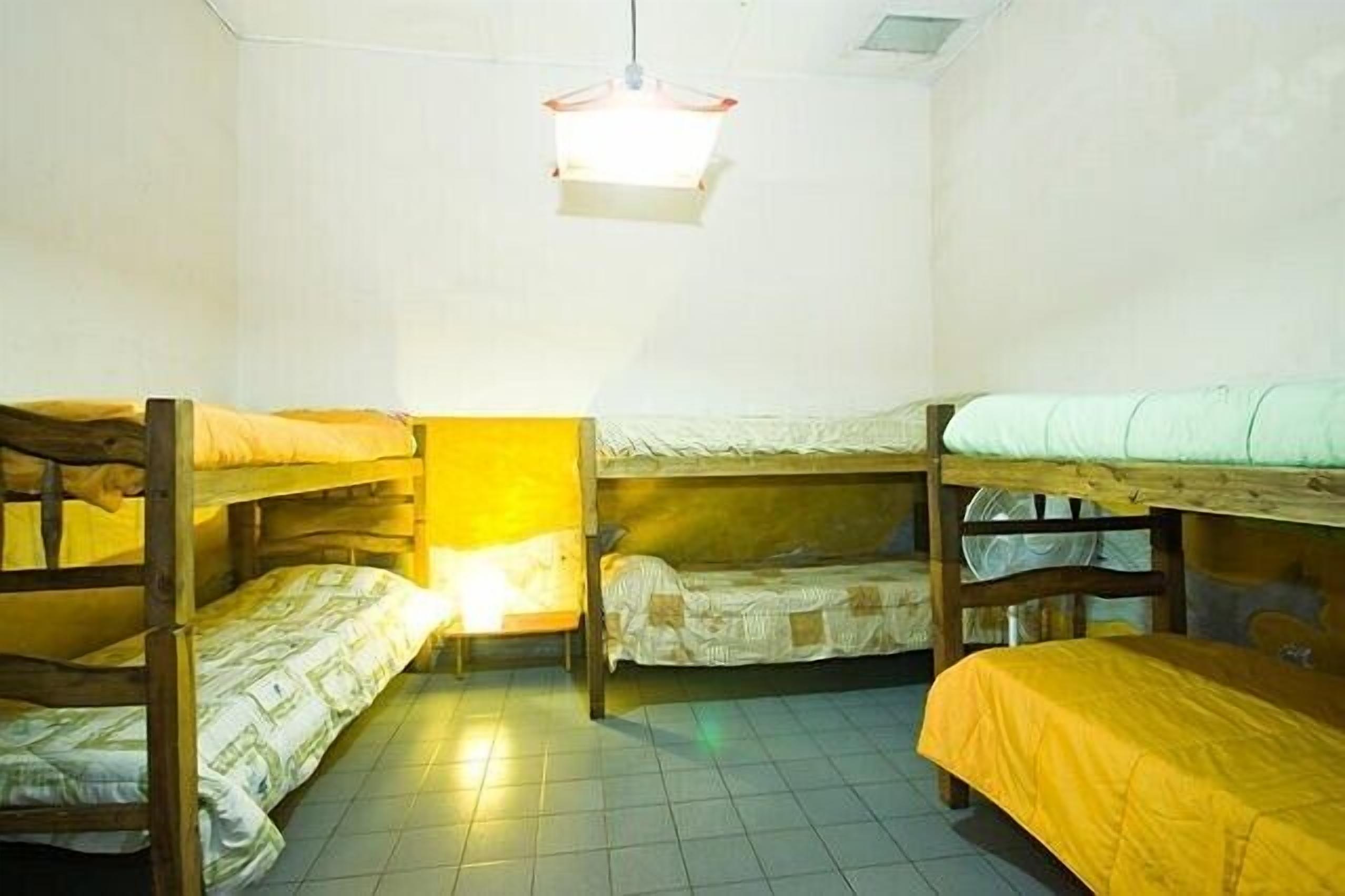 A dormitory room with bunk beds, a single bed, and a hanging light fixture.