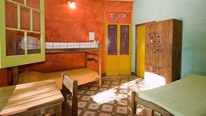 A room with two beds, a wooden table, a bench, a wardrobe, and a door with a decorative handle. - Casa Pueblo Hostel (Mendoza)