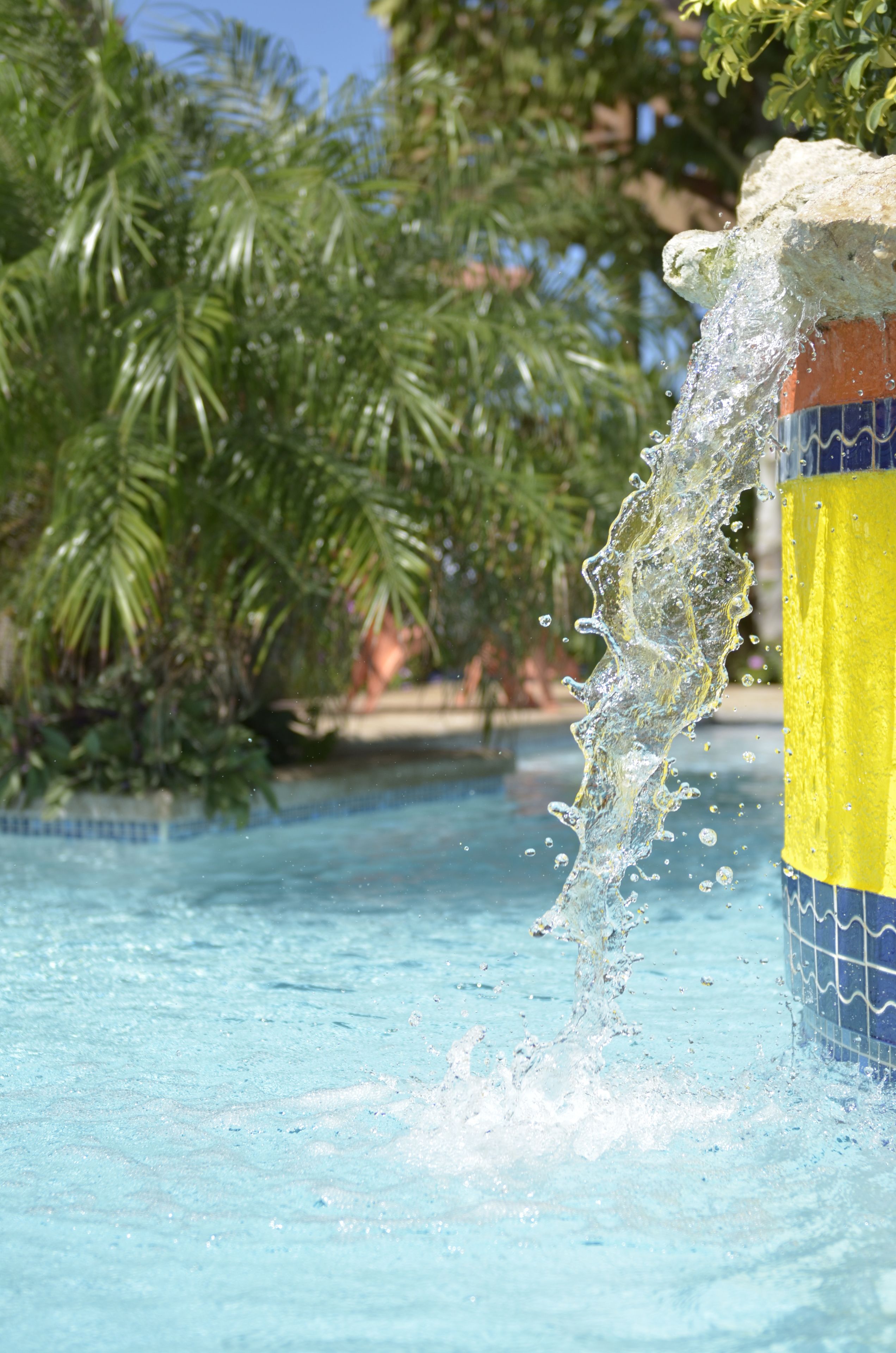 A clear view of a swimming pool with water splashing against a tiled pillar.