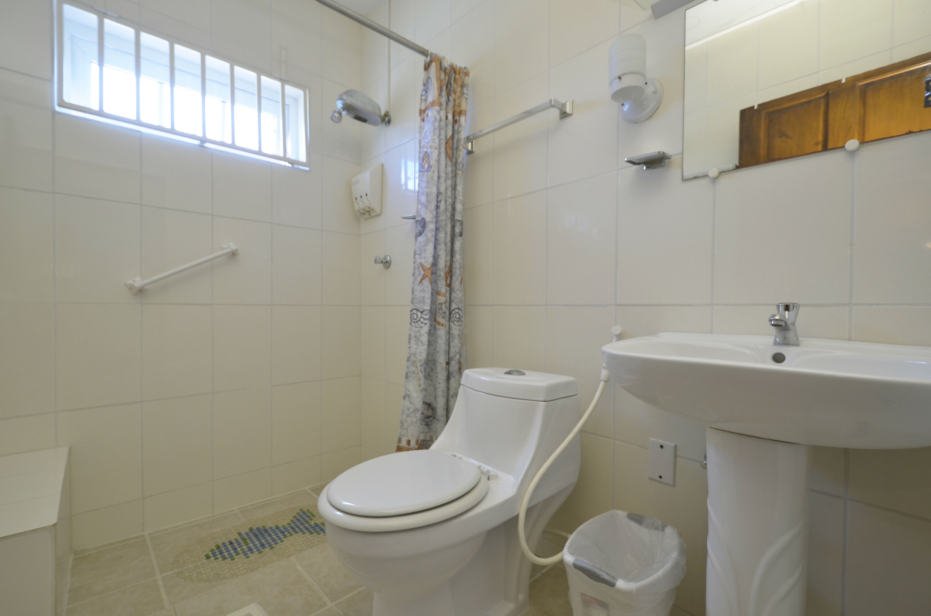 A bathroom with a toilet, a sink, a shower curtain, a window, and a mirror.