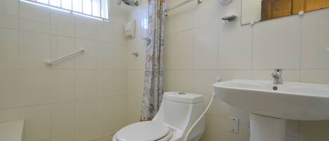 A bathroom with a toilet, a sink, a shower curtain, a window, and a mirror.